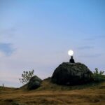 Silhouette observant le paysage au clair de lune pour repérer un lieu refuge, dans une nature calme et ouverte.