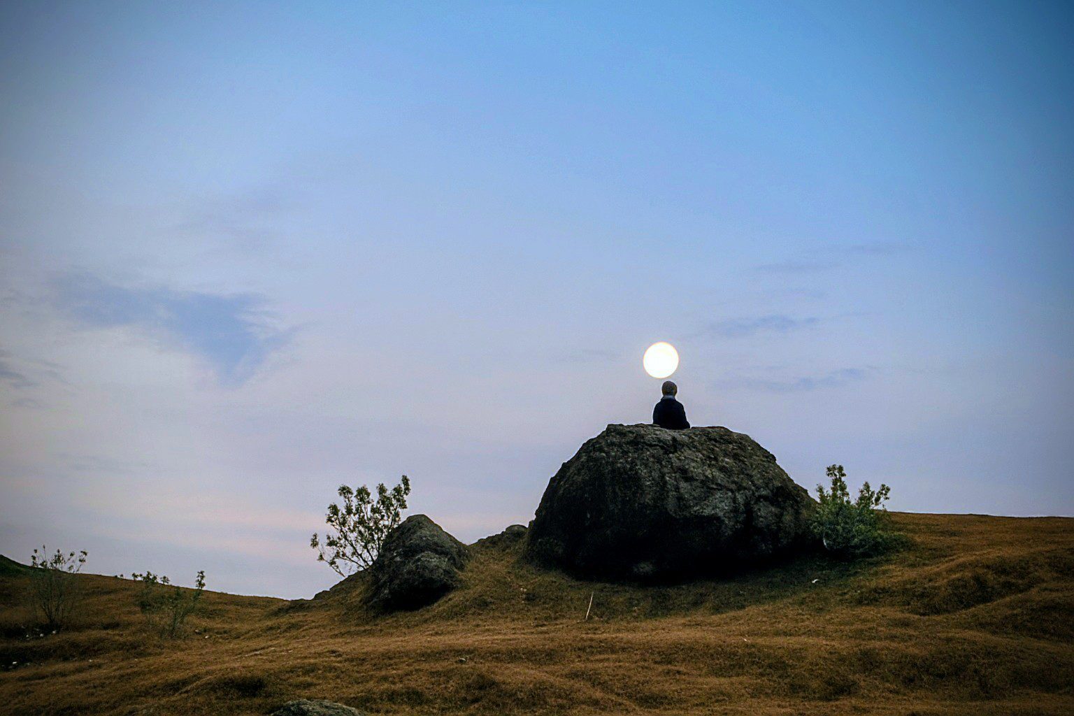 Silhouette observant le paysage au clair de lune pour repérer un lieu refuge, dans une nature calme et ouverte.