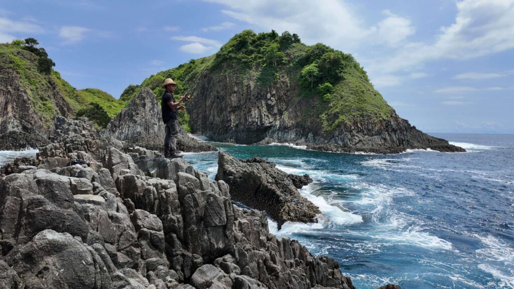Homme pêchant depuis la côte rocheuse en Asie du Sud-Est, symbole d’une vie simple et ancrée dans la nature